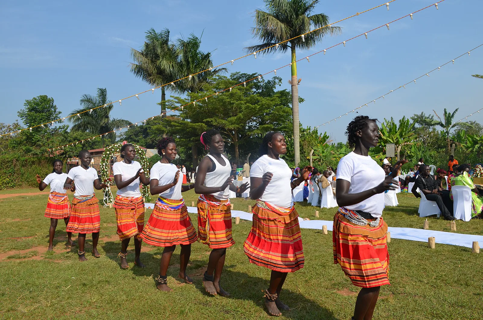 A line of Acholi women dancing in matching wraps on a grass field